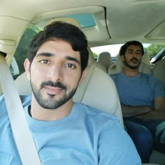 two men sitting in the back seat of a car, one with a beard and blue shirt