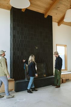 three people standing in front of a black wall with a clock on it's side