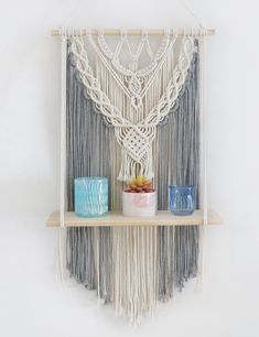 a macrame wall hanging on a shelf with candles and vases next to it