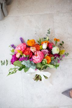 a bouquet of colorful flowers sitting on top of a white tile floor next to a pair of shoes