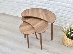 three wooden tables sitting next to a potted plant on the floor in front of a white brick wall