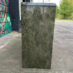 a trash can sitting on the sidewalk next to a wall with graffiti painted on it