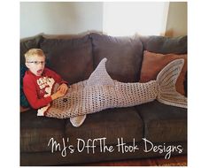 a young boy sitting on top of a couch next to a knitted shark blanket