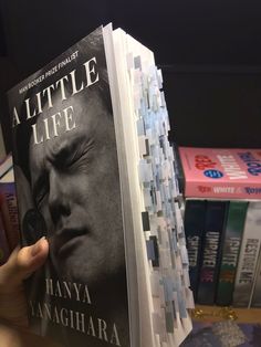 a person holding up a book in front of some books on a shelf with other books behind them