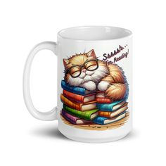 a white coffee mug with a cat wearing glasses on top of books and reading material