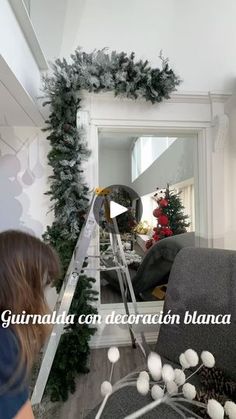 a woman standing in front of a mirror next to a christmas tree and garland on the wall