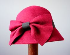 "DESCRIPTION * vintage hat from 1990s * Bucket style: round high crown with sloping downturned stiff brim * made with wool felt fabric * in deep red with a tint of purple * hatband is wrapped with a black grosgrain ribbon and embellished with a red bow * the bow can be worn to the side or to the back * tag reads \"One Size Body 100% Wool, Ribbon 100% Polyester\" CONDITION * Hat is in good clean condition with one spot of the insect bite mark, shown in the last photo. SIZE Hat circumference 22.5\ Retro Curved Brim Bucket Hat For Winter, Retro Winter Bucket Hat With Curved Brim, Winter Retro Curved Brim Bucket Hat, Retro Red Party Hat, Red Retro Party Hat, Vintage Cloche Hat For Winter, Vintage Winter Bucket Hat With Curved Brim, Winter Vintage Bucket Hat With Curved Brim, Curved Brim Winter Church Hat