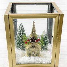 a small christmas village in a gold frame with pine cones and evergreens on top