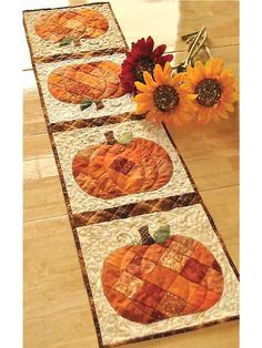 the table runner has four pumpkins on it and two sunflowers next to it