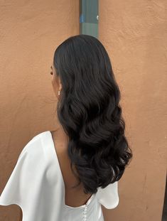 the back of a woman's head with long black hair in front of a tan wall