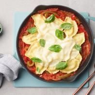 a skillet filled with pasta and sauce on top of a blue cutting board