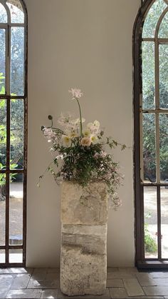 a vase filled with flowers sitting on top of a stone floor next to two windows