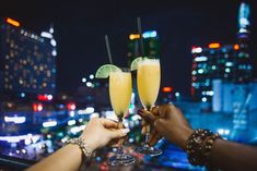 two people are toasting with drinks in front of a cityscape at night