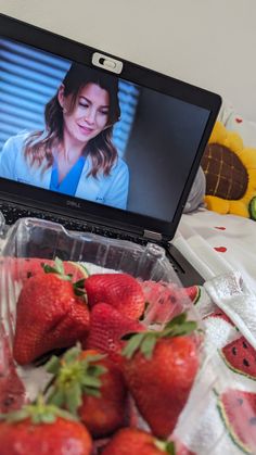 a laptop computer sitting on top of a bed with strawberries in front of it