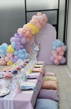 a table set up for a birthday party with pastel balloons and unicorns on it