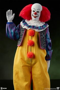 a clown with red hair and yellow pants is holding his hands up in the air