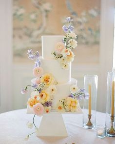 a three tiered cake with flowers on it sitting on top of a white table