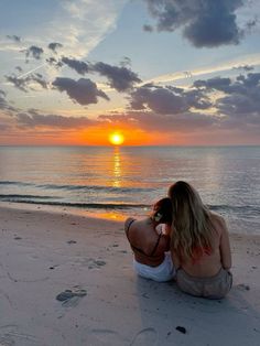 a woman is sitting on the beach talking on her cell phone while the sun sets