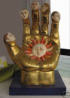 a golden hand statue with five heads on it's palm and the sun in the middle