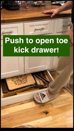 a person standing on top of a wooden floor next to a kitchen cabinet with the words push to open toe kick drawer