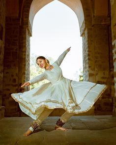 a woman is dancing in an archway with her arms out and legs spread wide as she stands on one leg