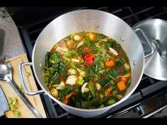 a pot filled with vegetables sitting on top of a stove next to a wooden cutting board