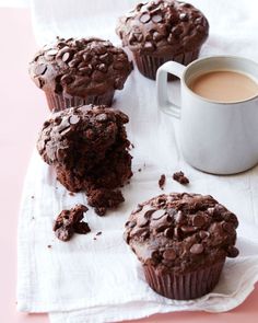 three chocolate muffins sitting on top of a napkin next to a cup of coffee