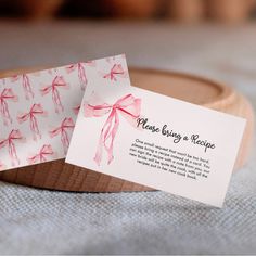 two business cards with pink bows on them sitting on a wooden stand next to a bowl