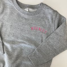 Choose from heather grey, navy, pink, black or royal, granite grey or white. Each sweatshirt is made from 60% cotton and 40% polyester. Each sweatshirt is embroidered with curved name in a small block font.  Please wash on cold and dry on low. If you are wanting a different design, more wording, or a different clothing style, please send me a message so we can discuss the details. In the notes to seller please enter the name/wording exactly how you would like it to read Click this link for white custom organic cotton t-shirts:  https://www.etsy.com/listing/988105502/organic-cotton-custom-name-embroidered?ref=shop_home_feat_1&pro=1&frs=1 If you need this order rushed, please add one of these  to your cart: Rush my order https://www.etsy.com/listing/1043569716/rush-my-order-for-t-shirts?ref= Heather Grey Embroidered Logo Sweatshirt For Winter, Heather Grey Winter Sweatshirt With Embroidered Logo, Gray Winter Sweatshirt With Embroidered Text, Winter Heather Grey Sweatshirt With Embroidered Logo, Gray Long Sleeve Top With Letter Embroidery, Gray Long Sleeve Top With Embroidered Text, Gray Long Sleeve Sweatshirt With Letter Embroidery, Gray Embroidered Winter Tops, Monogram Sweater