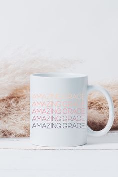 a white coffee mug with the words amazing grace on it sitting next to a furry animal