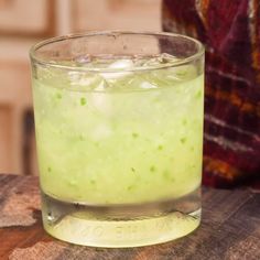 a glass filled with green liquid sitting on top of a wooden table