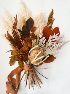 an arrangement of dried flowers and leaves on a white surface