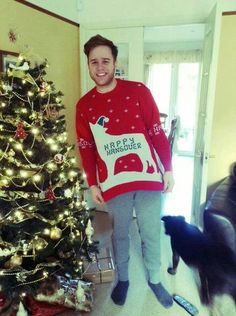 a man standing in front of a christmas tree next to a black and white dog