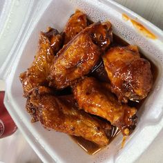 a plastic container filled with chicken wings covered in brown sauce next to a cup of ketchup