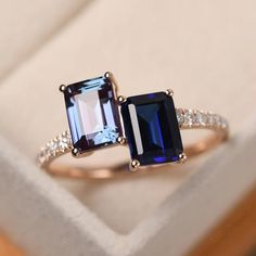 an engagement ring with two square cut blue sapphires and diamonds on the sides, sitting in a box