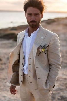 a man in a suit standing on the beach with his hands in his pockets and looking at the camera