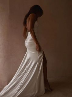 a woman in a long white dress standing next to a wall with her back turned