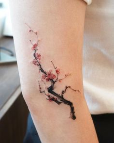 a woman's arm with a branch and flowers tattoo on the left side of her arm