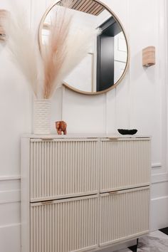 a white dresser topped with a mirror next to a tall vase filled with dry grass