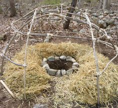 an outdoor fire pit made out of sticks and hay with rocks in the center surrounded by trees