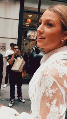 the woman is walking down the street with her hand in her pocket and wearing a white dress