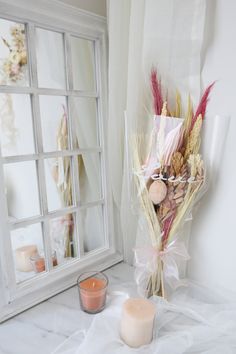 a vase filled with dried flowers next to a candle on a table near a window