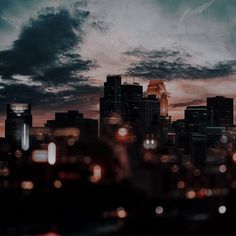 the city skyline is lit up at night, with clouds in the sky above it