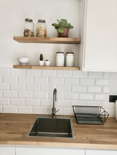 a kitchen sink with wooden counter tops and shelves above it, next to a white tiled backsplash