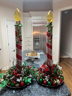 two christmas candles are sitting on a table in the middle of a kitchen with decorations