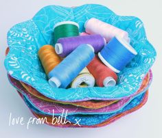 several spools of thread sit in a blue bowl on top of colorful fabrics