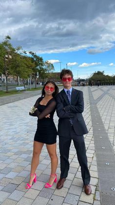 two people standing next to each other in front of a brick walkway with clouds overhead