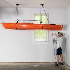 a man is holding on to an orange kayak hanging from the ceiling in a room