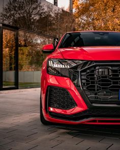 the front end of a red audi suv parked on a brick sidewalk in front of a building