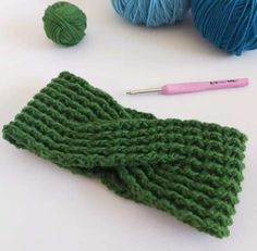 green knitted mitts and balls of yarn on a white surface with a pink crochet hook